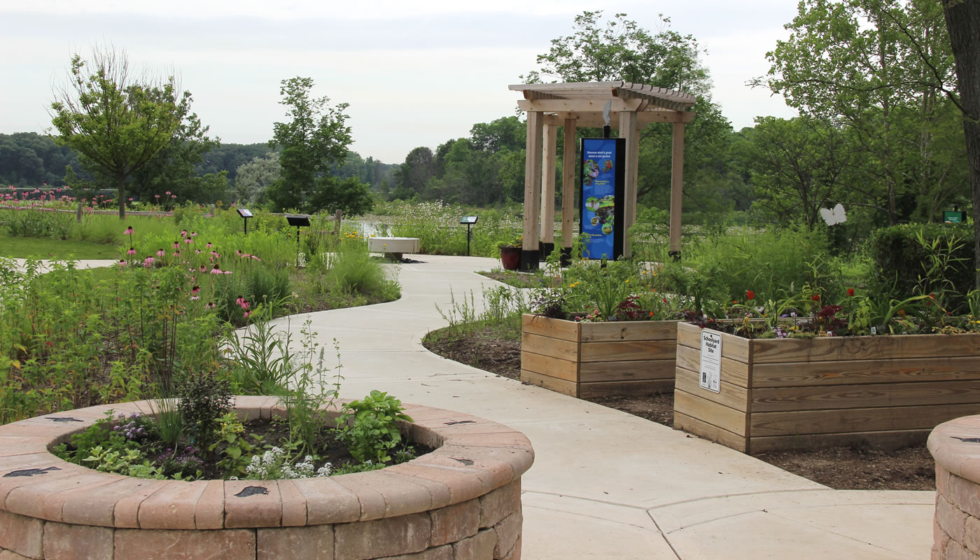 a garden with accessible raised beds, paved trail and interpretive signs