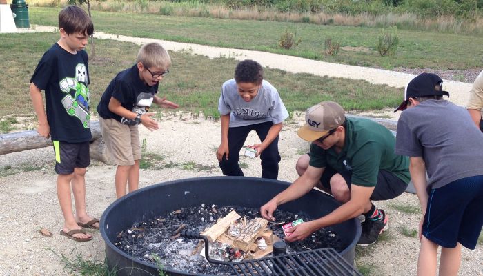 A Forest Preserves staff member showing how to light a fire in front of a small group at a Camping 101 event.