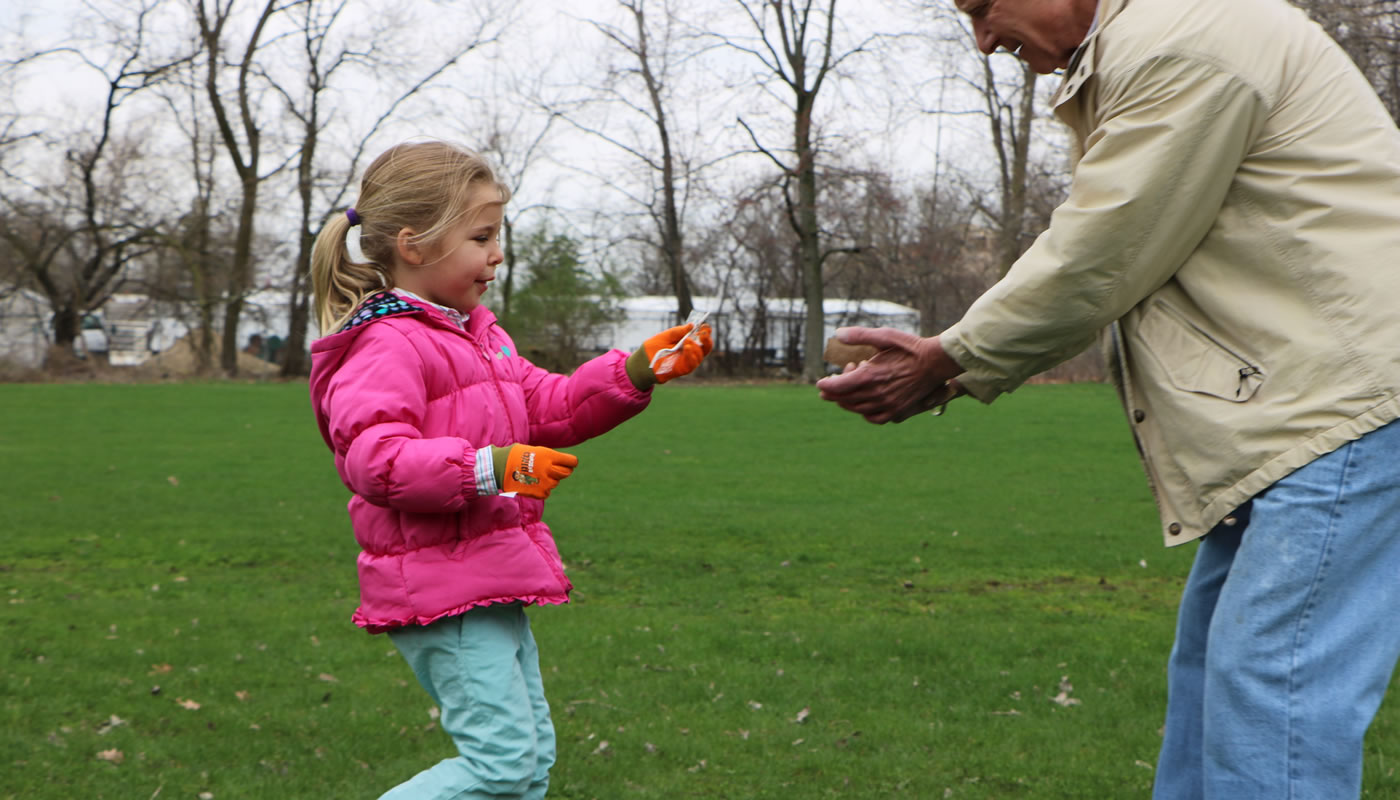 a young girl picks up trash in a picnic grove and hands it to her grandfather
