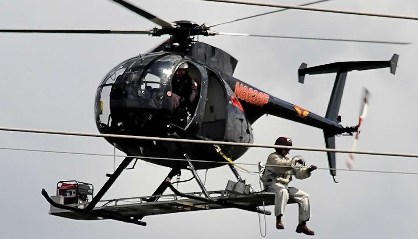 a helicopter hovering next to power lines while a person works on them