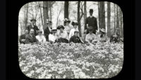 men and women sitting in a field of flowers around 1900