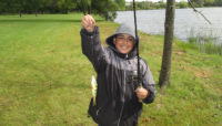 a boy holding up a fishing pole and fish in front of a lake