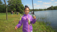 a girl holding up a fishing pole and fish in front of a lake