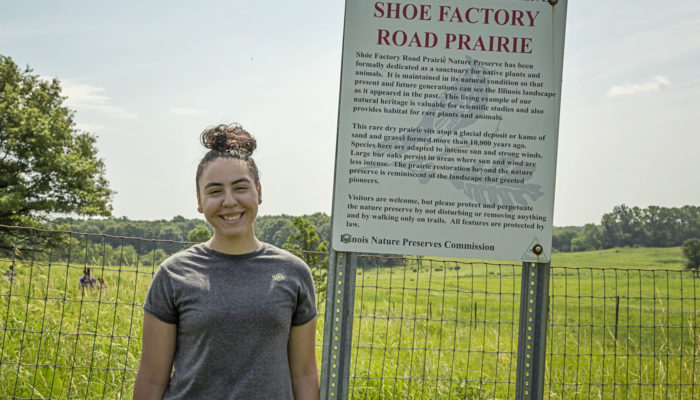 Leslie Gaeta standing in front of the sign at Shoe Factory Road Prairie