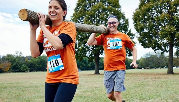 two people running while holding a log on their shoulders