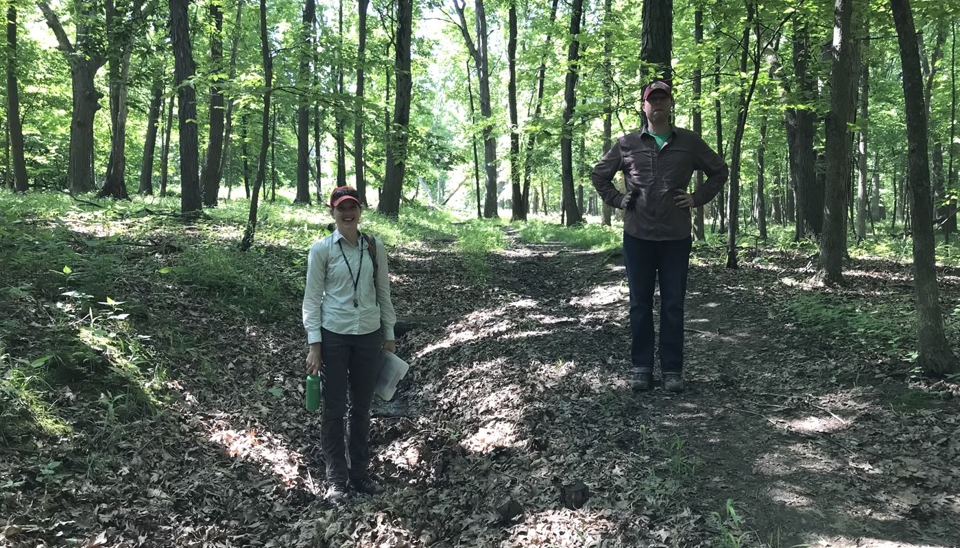 two Forest Preserves staff members, one standing on a trail, one standing below in an area with erosion issues