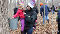 a mother and child exploring a sap bucket at River Trail Nature Center