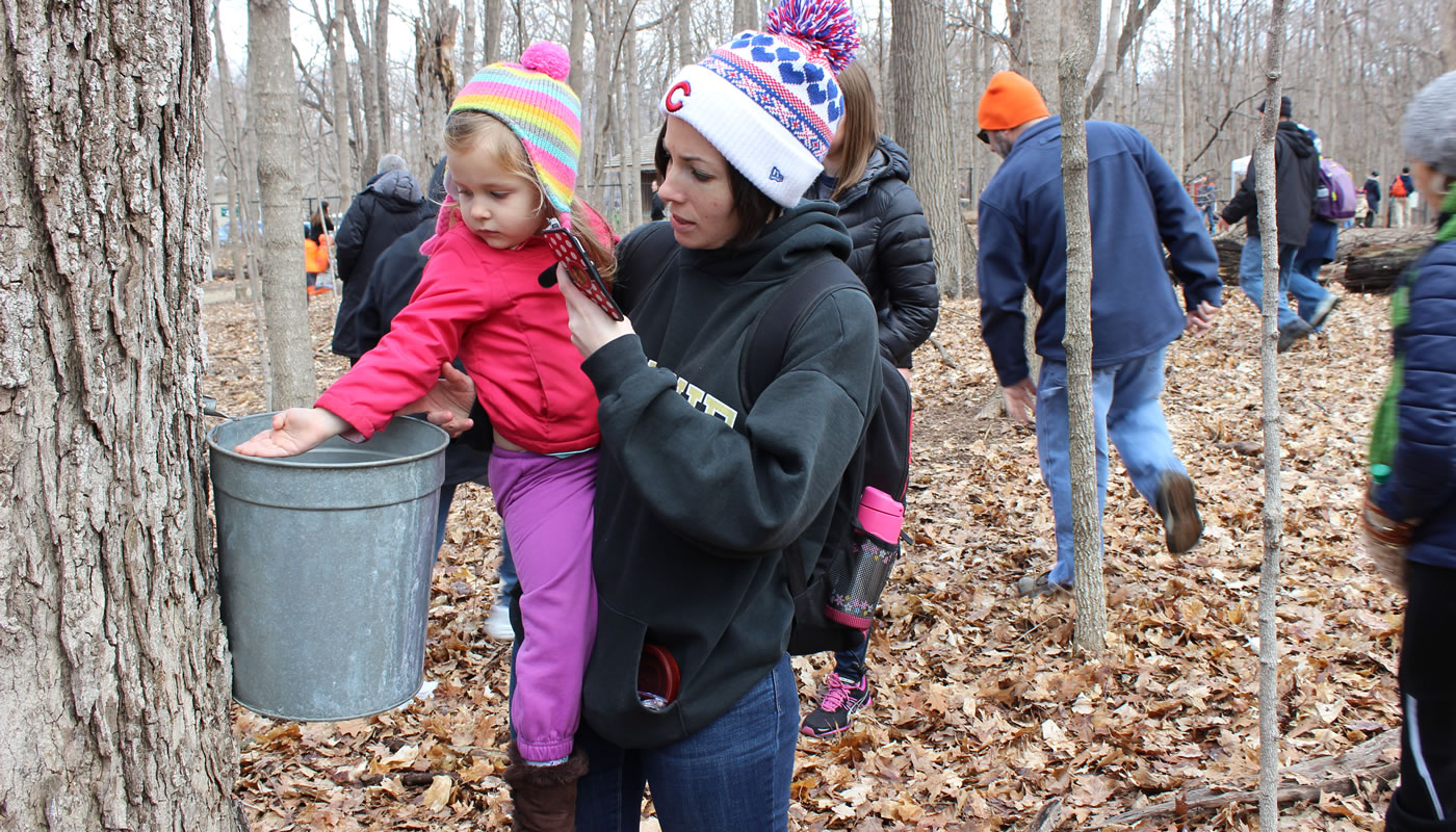 a mother and child exploring a sap bucket at River Trail Nature Center