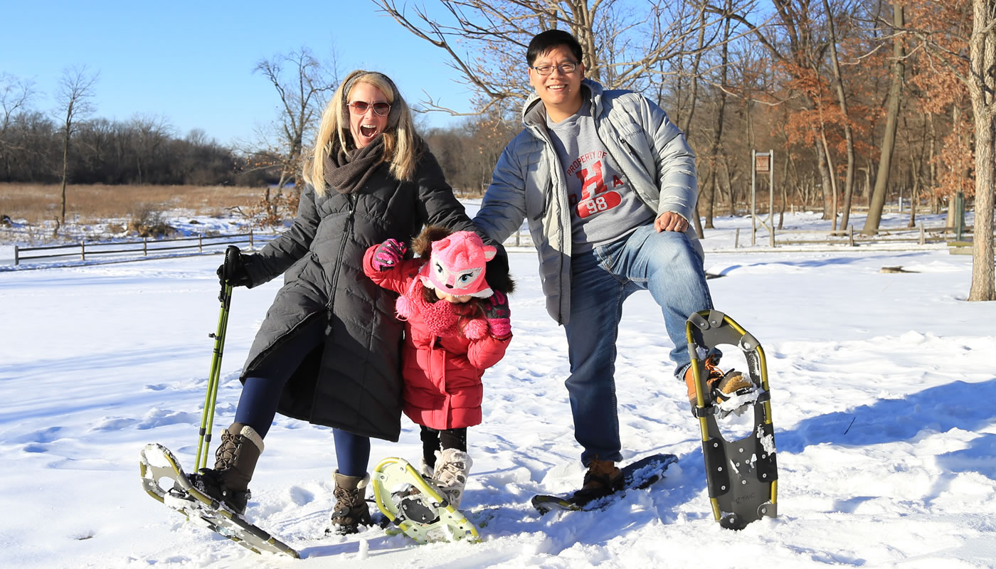 a family snowshoeing at trees and ground covered with snow at River Trail Nature Center