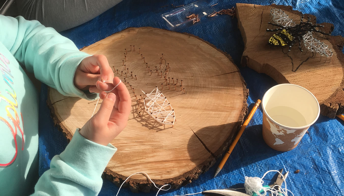 a person using string, nails and a slice of tree trunk to make art at Rolling Knolls Pavilion