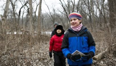 Three people walk in the woods during winter.