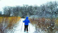 A visitor with snowshoes treks across a snowy path at Crabtree Nature Center.
