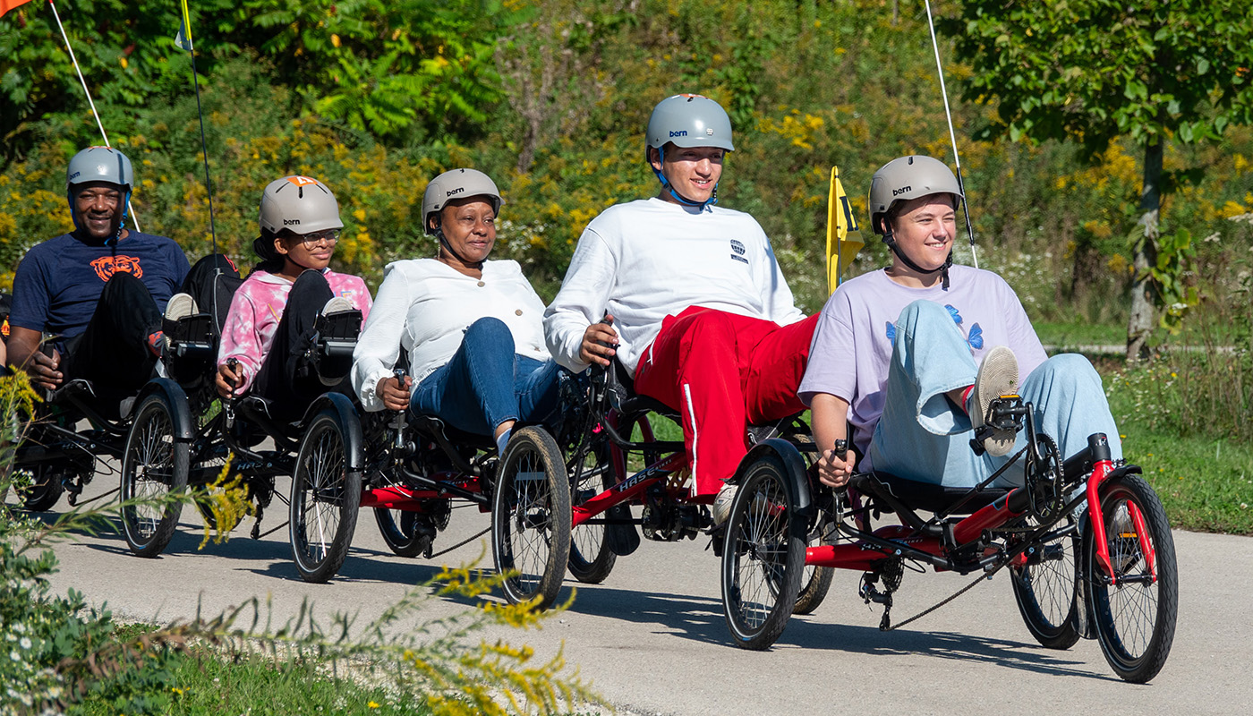 A group enjoying a ride on a forested trail using adaptive bicycles.