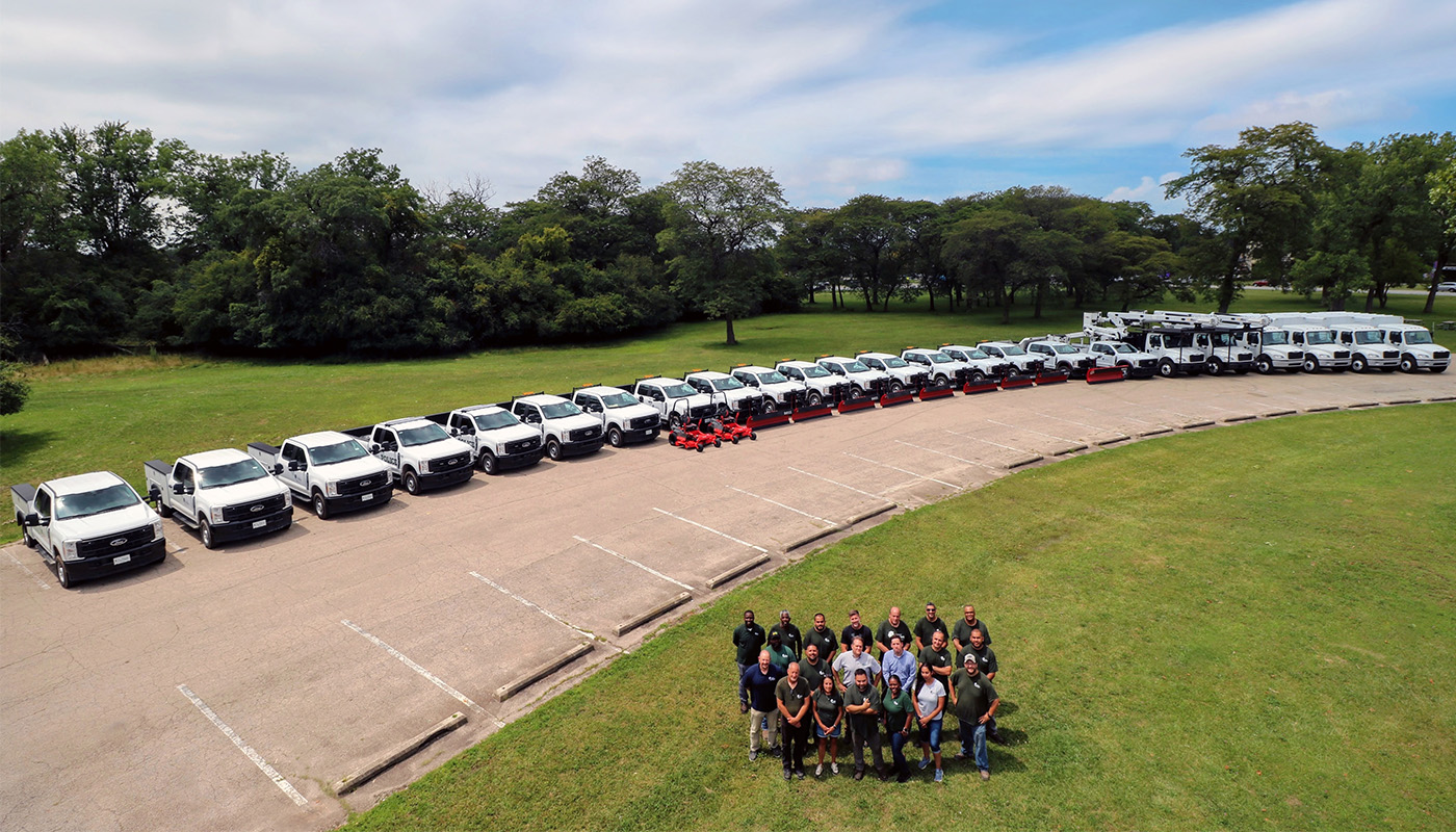 Facilities & Fleet Department staff posing in front of a wide array of Forest Preserves vehicles with a forest in the background.