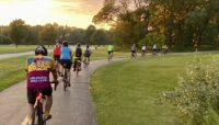 A group of biking riding on a paved trail in the woods.
