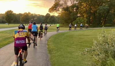 A group of biking riding on a paved trail in the woods.