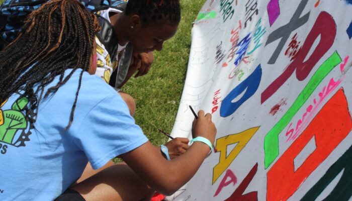 Teens drawing on a large poster at a teen exploration day event.