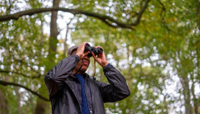 A man looking through binoculars in a forest.