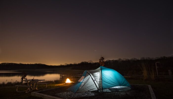 An illuminated camping tent at night near a lake.