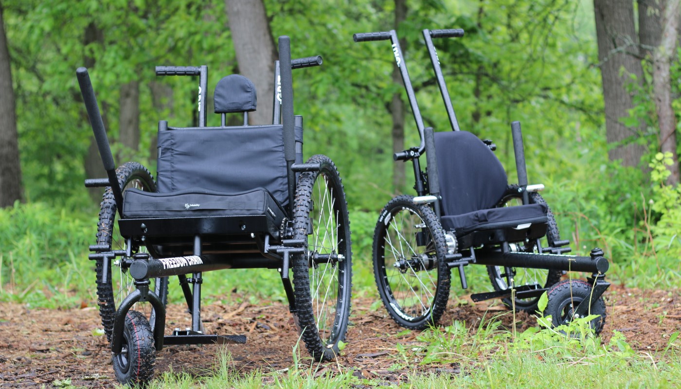 Two all-terrain wheelchairs outdoors.
