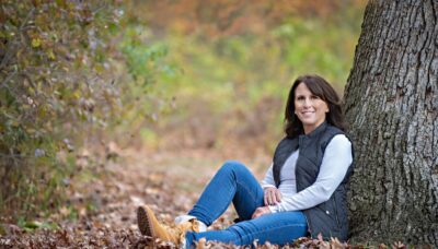 A woman is sitting next to a tree in the forest.