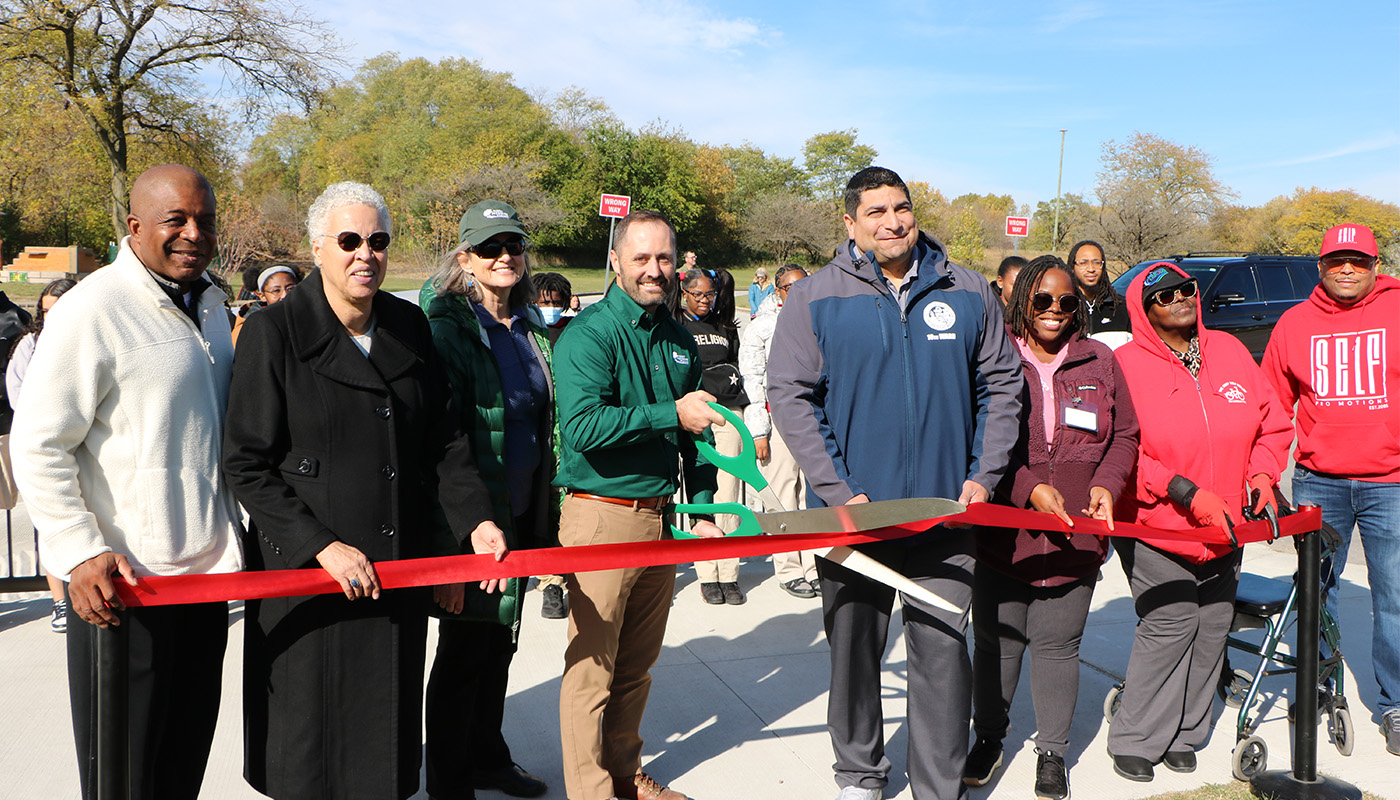 people about to cut into a ribbon with a large pair of scissors