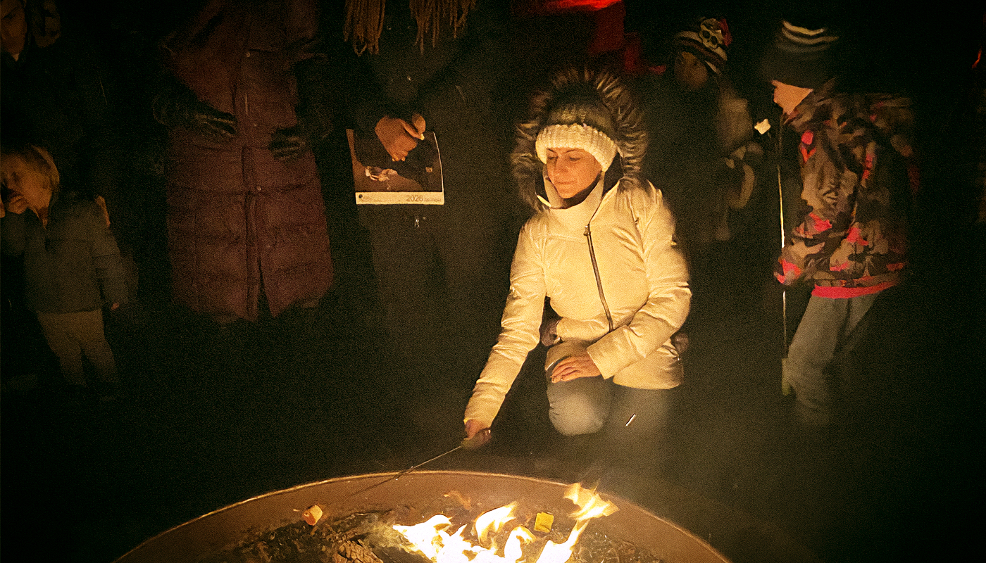 A group at an outdoor event surrounding a bonfire.