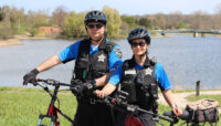 two police officers standing next to their bicycles in front of a lake