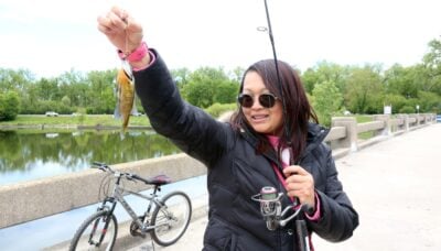 A woman holding a fish and fishing pole outdoors.