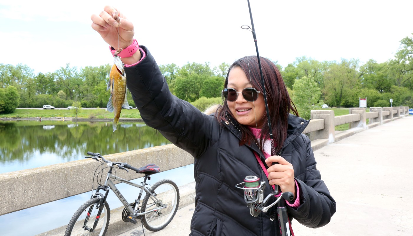 A woman holding a fish and fishing pole outdoors.