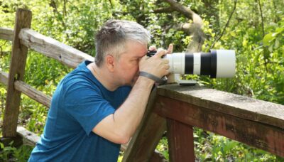 A person taking a photograph with a large camera lens outdoors.