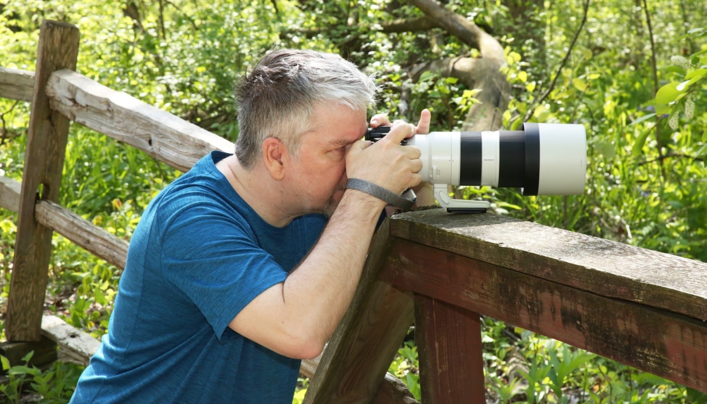A person taking a photograph with a large camera lens outdoors.